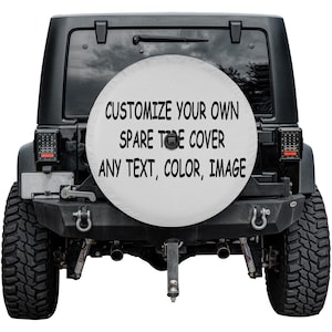 May include: A black Jeep SUV with a white spare tire cover. The cover features the text "CUSTOMIZE YOUR OWN SPARE TIRE COVER ANY TEXT, COLOR, IMAGE" in black. The vehicle has large, black tires and a black bumper.