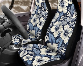 May include: Car seat covers featuring a floral pattern of large white hibiscus flowers and blue leaves on a navy blue background. The covers are installed in a car, with the steering wheel visible.