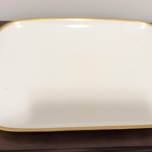 May include: A white square serving platter with a gold trim around the edge.