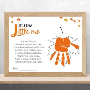 Puede incluir: Una impresión enmarcada con las palabras "LITTLE LEAF Little me" en escritura naranja. La impresión presenta una huella de mano naranja en forma de hoja y un poema. El marco es de madera marrón claro.