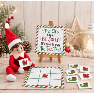 May include: A plush elf doll in a red suit and hat sits next to a tic-tac-toe game set. The game includes a square board with a red and green striped border, small game pieces featuring elf shoes and mittens, and a sign that reads The Elf says... BE JOLLY It's time to play TIC TAC TOE! displayed on a wooden easel.