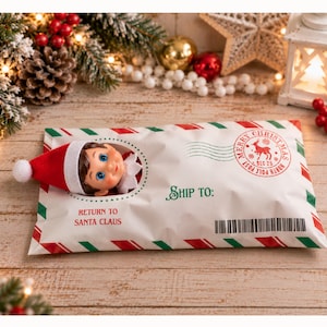 Pode incluir: Um envelope de envio branco com listras diagonais vermelhas e verdes nas bordas. O envelope apresenta um recorte circular mostrando uma boneca com um chapéu vermelho e olhos azuis. O texto diz: SHIP TO:, RETURN TO SANTA CLAUS, MERRY CHRISTMAS.