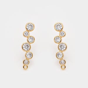 May include: A pair of gold-colored earrings with a cascading design. Each earring features a series of clear, round gemstones of varying sizes, set in individual bezels. The earrings have a post and loop closure.