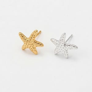 May include: A pair of starfish stud earrings, one gold-toned and one silver-toned, against a white background. The earrings are small, with textured surfaces, and are designed to be worn in pierced ears. The starfish design is a popular motif for beach-themed jewelry.