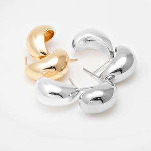 May include: A pair of gold-toned and a pair of silver-toned teardrop-shaped stud earrings. The earrings are arranged on a white surface. The earrings have a smooth, polished finish and a post backing.