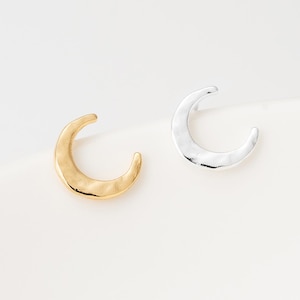 May include: Two crescent moon shaped earrings, one in a polished gold tone and one in a polished silver tone. Each earring features a smooth, slightly hammered texture with a curved design that mimics the shape of a waxing crescent moon.