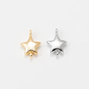 May include: Two star-shaped charms, one gold-colored and one silver-colored, are displayed against a white background. Each charm has a loop at the top and a small post at the bottom, suggesting they are designed for jewelry making or crafting.