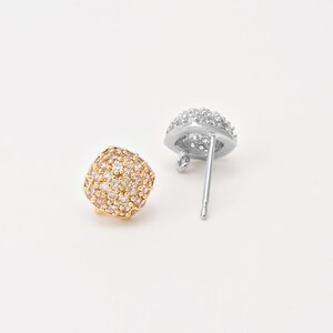 May include: Two stud earrings featuring a rounded square shape covered in small clear crystals. One earring is finished in a warm gold tone, while the other is finished in a silver tone, showing the metal post and a small loop on the back.