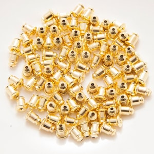 May include: A pile of gold-coloured metal earring backs on a white plate.