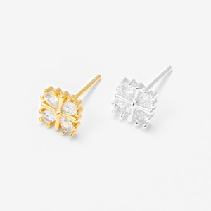 May include: Two stud earrings, one gold-toned and one silver-toned, each featuring a four-leaf clover design. The clover petals are made of clear, sparkling stones. The earrings are displayed on a white background.