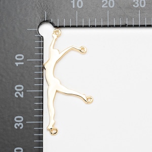 Puede incluir: Un dije de metal dorado con forma de bailarina, con los brazos extendidos y una pierna extendida. El dije tiene tres pequeños bucles para sujetarlo a otros componentes de joyería. El dije mide aproximadamente 3,8 cm de largo.