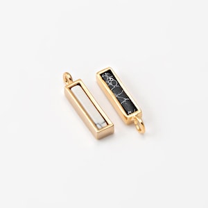 May include: Two rectangular gold-colored pendants. One pendant features a white stone, and the other has a black and white patterned stone. Each pendant has a small loop at the top for attaching to a chain or other jewelry component.