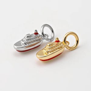 Könnte beinhalten: Zwei silberne und goldene Anhänger in Form eines Kreuzfahrtschiffs mit roten Akzenten. Die Anhänger sind so konzipiert, dass sie an ein Armband oder eine Halskette angebracht werden können.