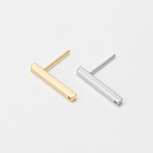 May include: Two minimalist bar stud earrings. One is gold-colored, the other is silver-colored. Both earrings have a rectangular bar design with a post for piercing. The earrings are displayed on a white background.