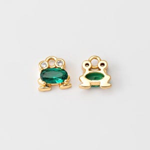May include: Two gold frog charms with green gem accents. One charm has clear rhinestones on the head.