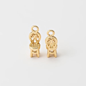 Puede incluir: Dos pequeños dijes dorados con forma de silla. Cada dije presenta un respaldo detallado con un diseño calado y un pequeño asiento. Los dijes son réplicas en miniatura de un diseño de silla clásico.