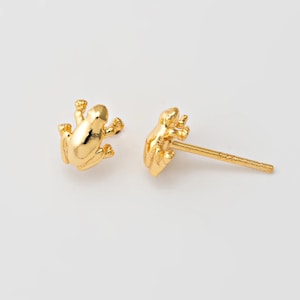 May include: A pair of gold frog stud earrings. The frog is facing forward with its legs outstretched.