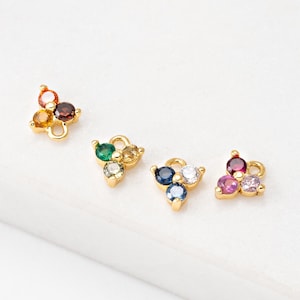 Puede incluir: Cuatro abalorios triangulares de oro con piedras preciosas de diferentes colores. Cada abalorio tiene tres piedras preciosas en forma de triángulo. Las piedras preciosas son verdes, azules, rosas y marrones.