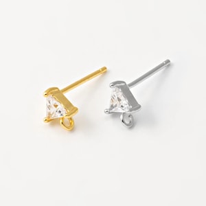 May include: Two stud earrings, one gold-toned and one silver-toned, each featuring a clear, triangular gemstone. The earrings have a post for insertion and a small loop at the bottom. The background is a plain white.