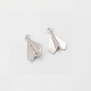 以下が含まれることがあります： 2つの銀色の紙飛行機のチャーム。各チャームの上部には、チェーンやその他のジュエリーコンポーネントに取り付けるためのループが付いています。紙飛行機のデザインはシンプルでモダンで、翼が折りたたまれています。