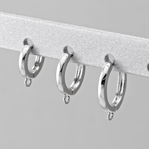 May include: Three silver hoop earrings with a small drop dangle on each earring.