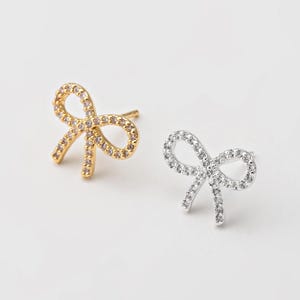 May include: A pair of bow-shaped earrings with a pave setting of clear cubic zirconia stones. One earring is gold-toned and the other is silver-toned.