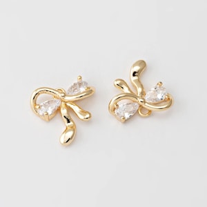 Op de afbeelding: Twee goudkleurige strik-charms met heldere kristallen accenten. De charms hebben een delicaat, vrouwelijk ontwerp en zijn perfect om een ​​toets van glans toe te voegen aan sieradenprojecten.