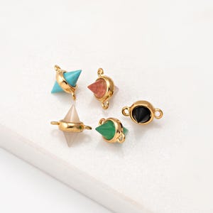 May include: Five gold-coloured jewellery components with gemstone accents. Gemstones include turquoise, pink, clear, green, and black. Each component has a unique shape and design, suitable for jewellery making.