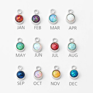 Puede incluir: Doce abalorios de plata con piedras preciosas de diferentes colores, cada uno representando un mes del año. Enero es rojo, febrero es morado, marzo es blanco, abril es blanco, mayo es verde, junio es blanco, julio es rojo, agosto es blanco, septiembre es azul, octubre es blanco, noviembre es amarillo y diciembre es azul.