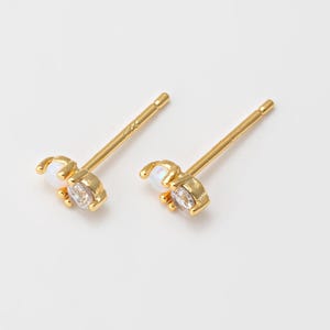 May include: A pair of gold stud earrings with a small white opal and a clear rhinestone.