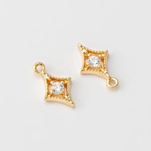 May include: Two gold-tone metal charms with a clear rhinestone in the center. Each charm is shaped like a diamond with a loop at the top for attaching to jewelry.