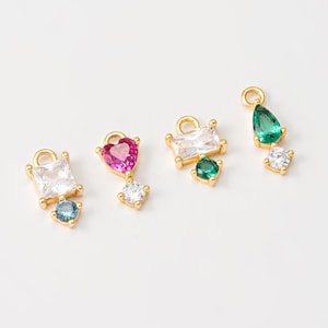 May include: Four gold charm pendants with different colored gemstones. Each charm features a clear crystal and a colored gemstone: blue, green, pink, and green. The charms are perfect for adding a touch of sparkle to jewelry projects.
