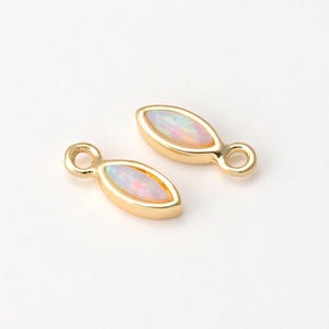 May include: Two gold-colored, marquise-shaped jewelry findings with iridescent opal-like centers. Each finding has a small loop at one end. The findings are set against a white background.