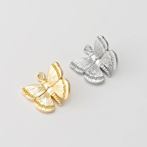 Puede incluir: Dos abalorios de mariposa, uno dorado y otro plateado, con alas detalladas y un bucle para sujetar a las joyas.