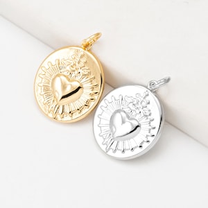 May include: Two pendant necklaces, one gold-toned and one silver-toned. Each pendant features a heart design at the center, surrounded by a sunburst pattern. The pendants are oval-shaped with a loop at the top for a chain.