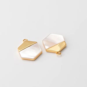 May include: Two gold and white hexagonal pendant charms with a loop for attaching to jewelry. The charms are made of metal and have a white shell inlay.