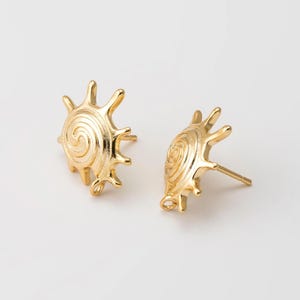 Puede incluir: Un par de pendientes de color dorado con un diseño de sol. Cada pendiente presenta un patrón en espiral en el centro.