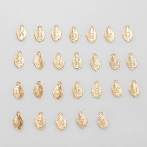 May include: Gold-colored leaf-shaped charms with engraved letters A through V. Each charm has a small loop at the top for attaching to jewelry. The charms are arranged on a white background.