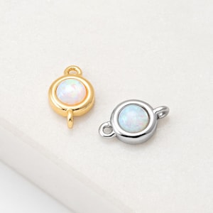 Puede incluir: Dos conectores de joyería con piedras de ópalo redondas. Un conector es de color dorado con un lazo y un poste. El otro conector es plateado con dos lazos. Ambos tienen una piedra de ópalo blanca e iridiscente.