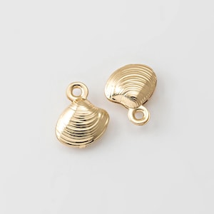 May include: Two gold-colored seashell charms with a textured surface and a small loop at the top for attaching to jewelry. The charms are set against a white background.