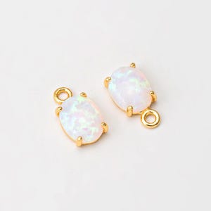 May include: Two gold oval-shaped charms with white opal stones. Each charm has a jump ring for attaching to jewelry.