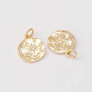 Puede incluir: Dos colgantes celestiales dorados. Cada colgante es redondo con una superficie texturizada, con estrellas y un diseño de luna creciente. Uno tiene un borde de pequeños cristales transparentes. Ambos tienen un pequeño lazo.