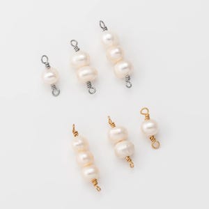 May include: Overhead shot of several pearl beads with silver and gold wire detailing. The pearls are white and vary in size, strung together in small clusters. The background is a plain white surface.