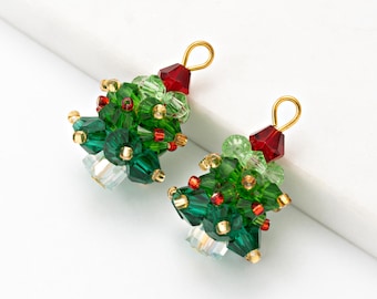 May include: Two Christmas tree-shaped earrings. Each earring is made of green, red, and clear crystal beads, with gold-colored accents. The earrings have a gold-colored loop at the top for hanging.