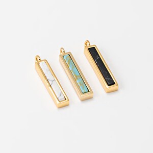 May include: Three rectangular pendants with gold-colored frames. Each pendant features a different stone: white with gray veining, turquoise, and black. The pendants have a small loop at the top for hanging.