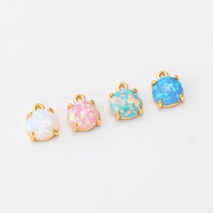 May include: Four gold-tone charms with opal-like stones in different colors: white, pink, blue, and light blue. The charms have a loop at the top for attaching to jewelry.