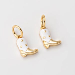 May include: A pair of gold-colored cowboy boot earrings with white enamel and star details. The earrings are on a white background.