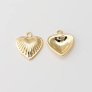 Puede incluir: Dos abalorios en forma de corazón de color dorado con un diseño texturizado. Un abalorio tiene una superficie lisa, mientras que el otro tiene un diseño acanalado.