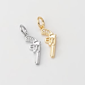 May include: Two silver and gold charm pendants in the shape of a revolver with small clear rhinestones on the barrel.