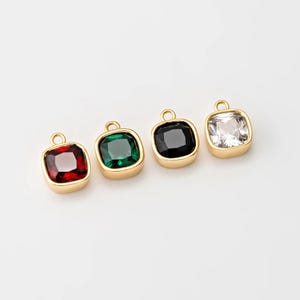 May include: Four gold-toned charms with square-shaped, faceted glass stones. The stones are red, green, black, and clear.